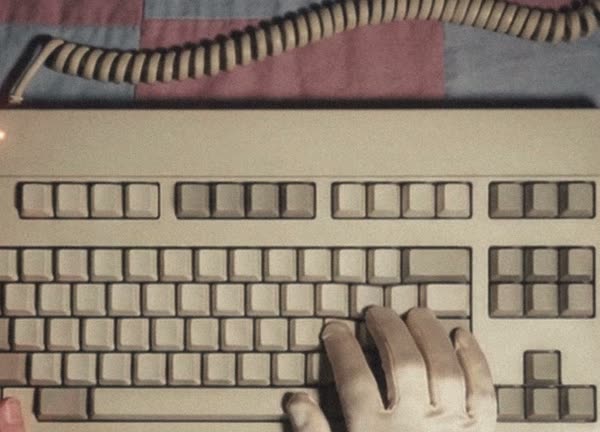 A gloved hand and a bare hand on a beige keyboard